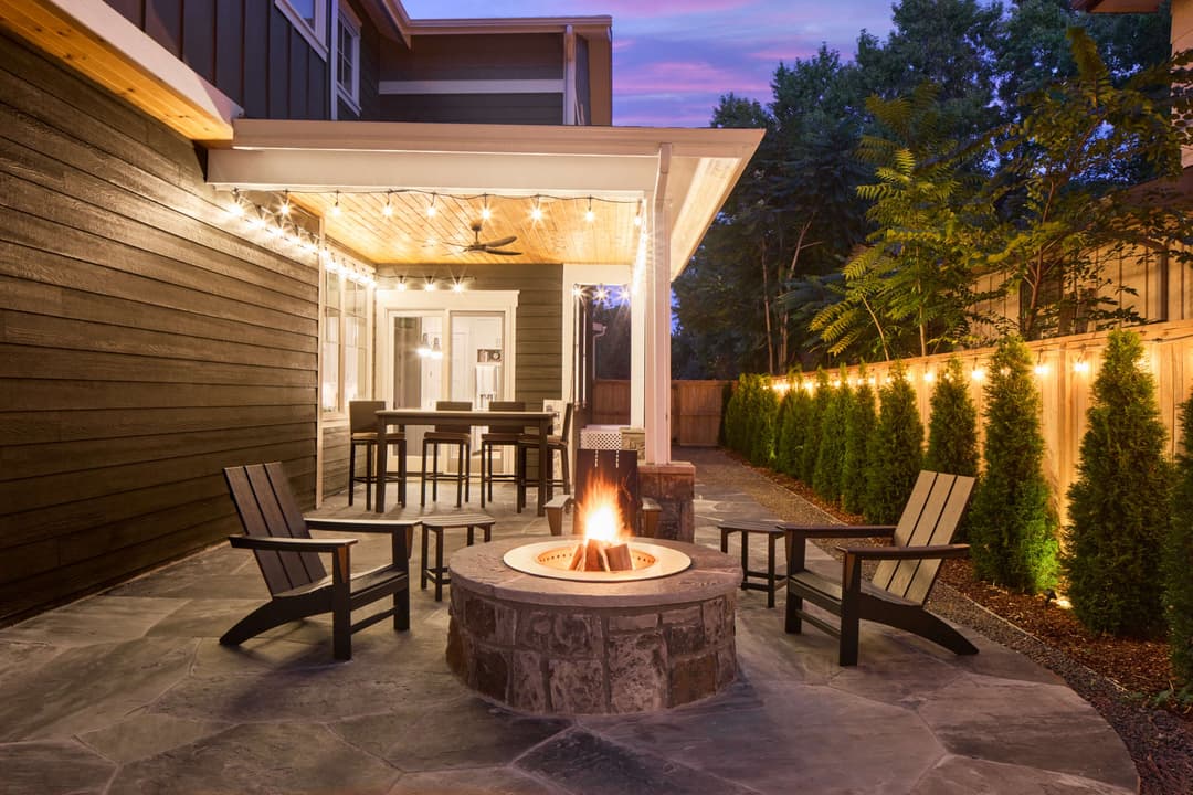 Cozy outdoor patio with a fire pit, wooden chairs, and string lights at dusk.