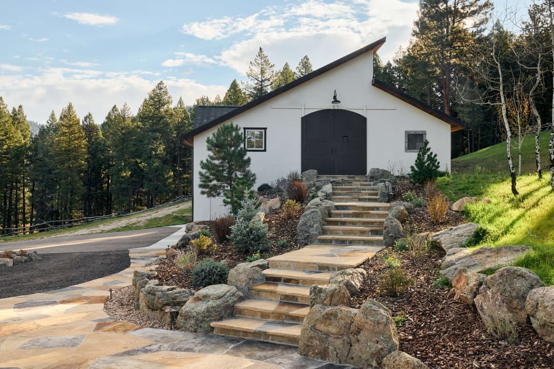 Modern white barn-style building surrounded by lush greenery and stone pathways.
