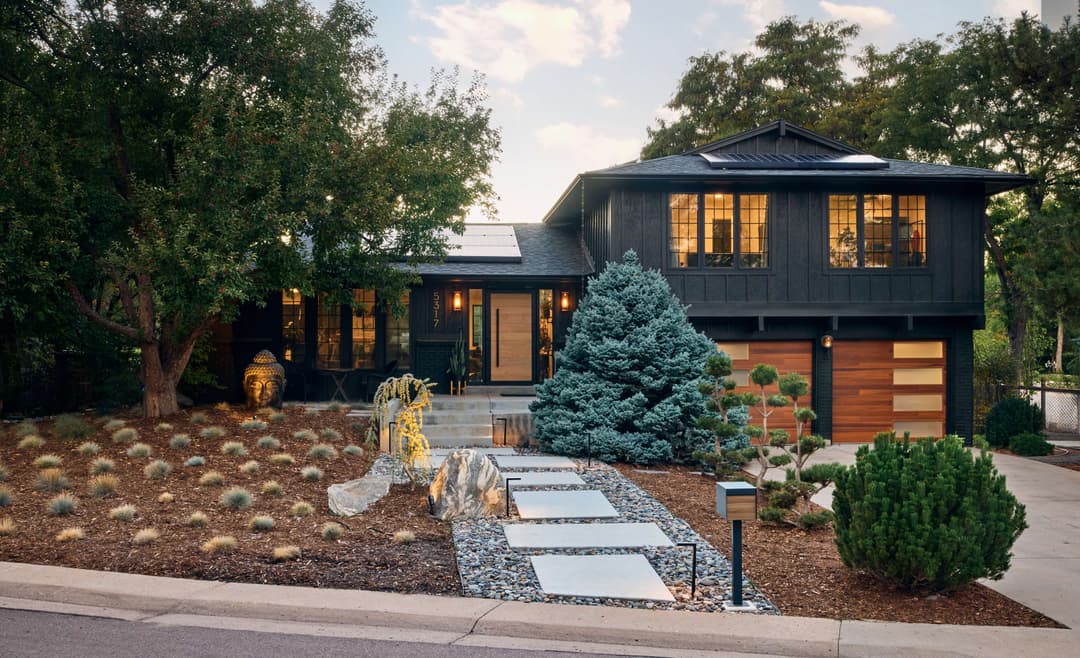 Modern black house with solar panels, landscaped yard, and stylish pathways.