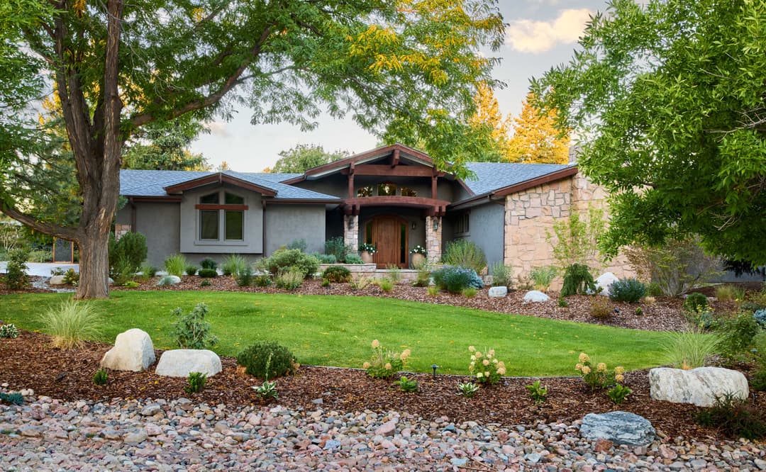 Modern ranch-style home with stone accents, lush landscaping, and vibrant greenery.