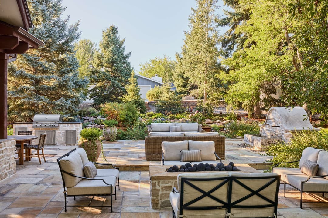 Elegant outdoor patio with seating, fireplace, and lush greenery in a serene garden setting.