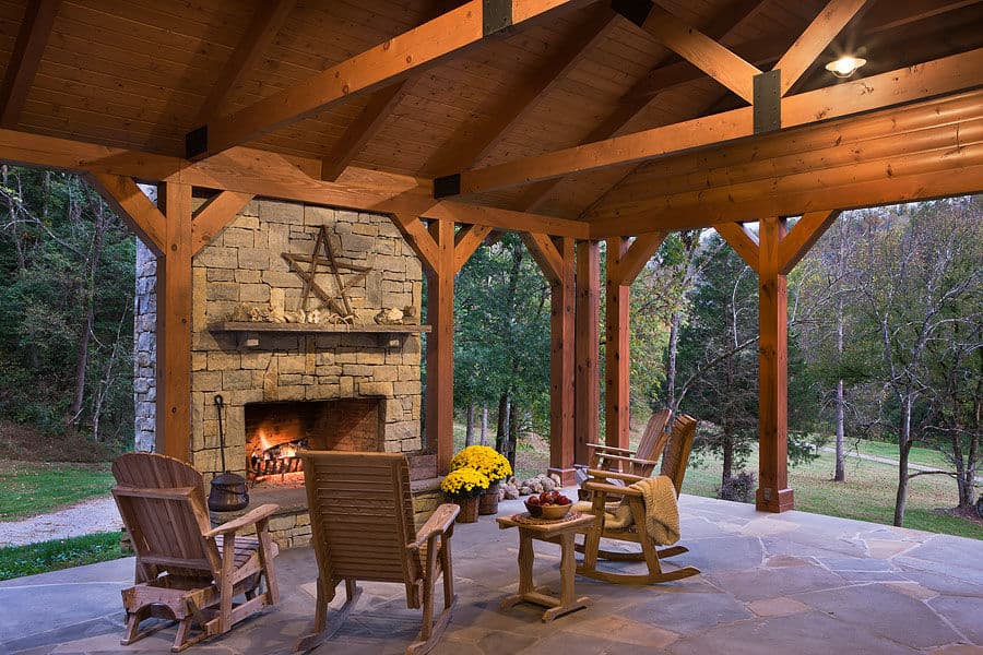 Cozy outdoor patio with a stone fireplace, wooden chairs, and colorful autumn plants.