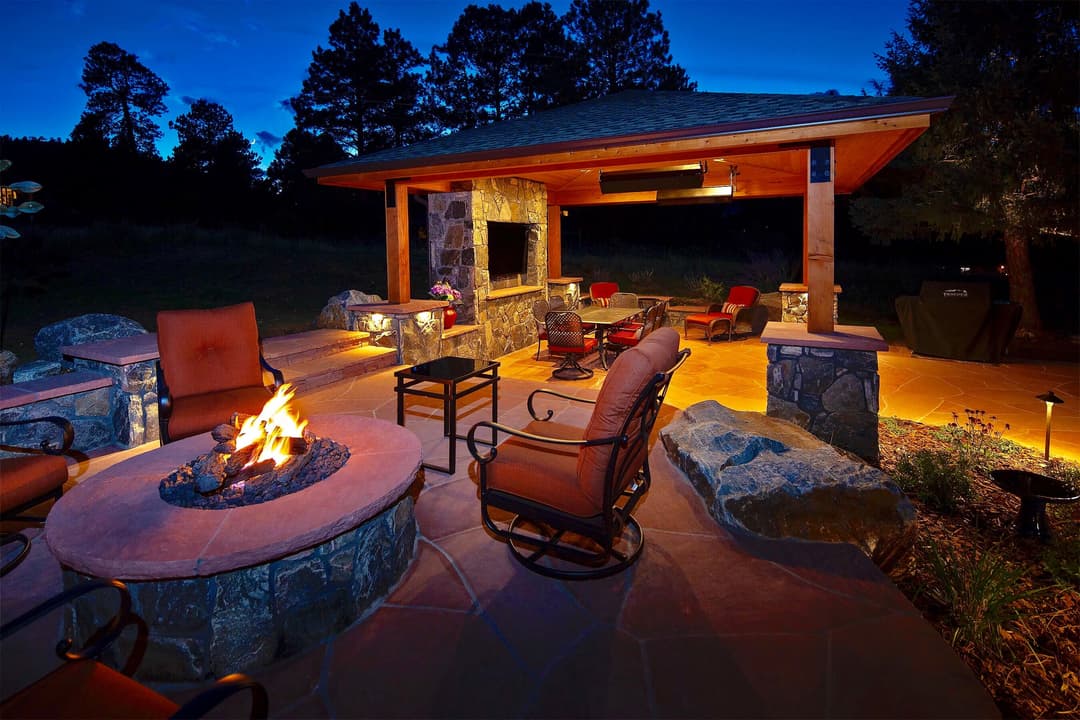 Cozy outdoor living space with a stone fire pit, seating, and ambient lighting at dusk.