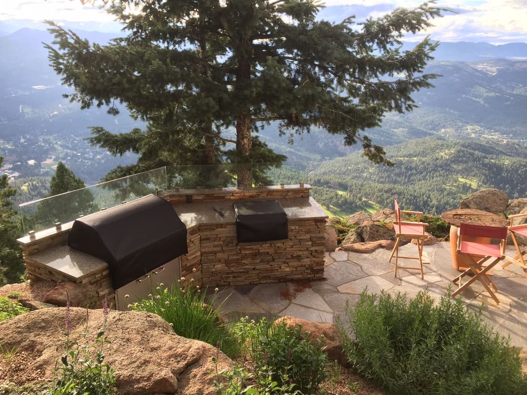 Scenic mountain view with an outdoor grill and dining area, surrounded by greenery.