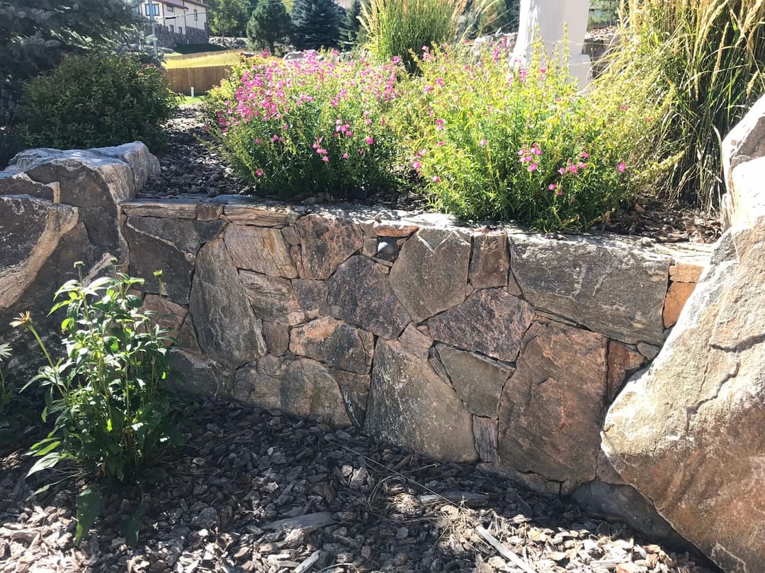 Rock wall garden with flowers and greenery set in a landscaped outdoor area.