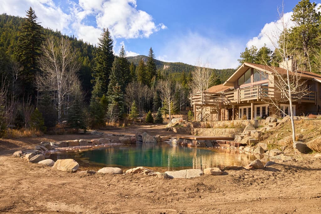 Scenic mountain retreat with hot springs pond and modern wooden lodge surrounded by nature.