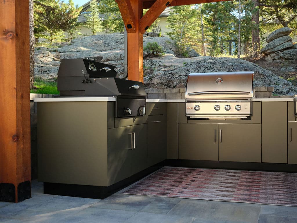 Modern outdoor kitchen with grill and cabinets under wooden gazebo in scenic natural setting.