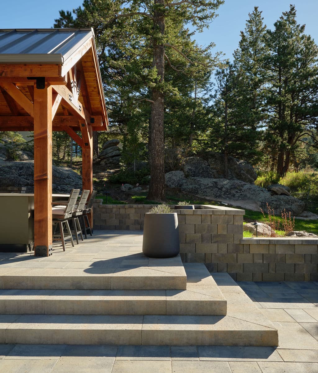 Outdoor patio with stone steps, a modern planter, and a wooden gazebo surrounded by trees.