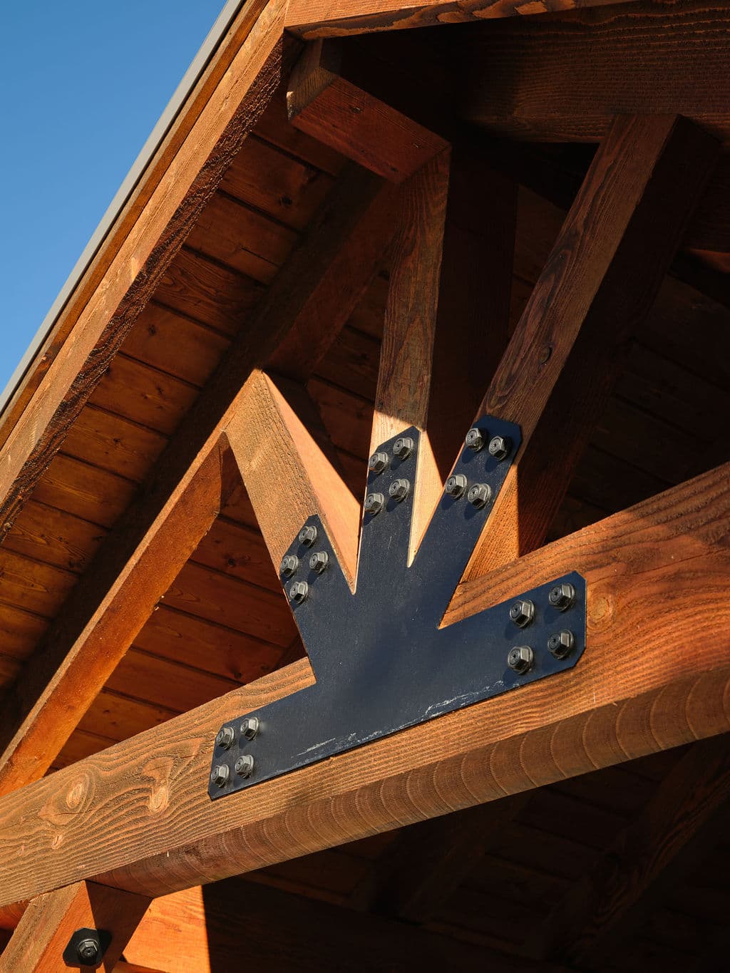 Wooden roof structure featuring decorative black metal support brackets against a clear blue sky.