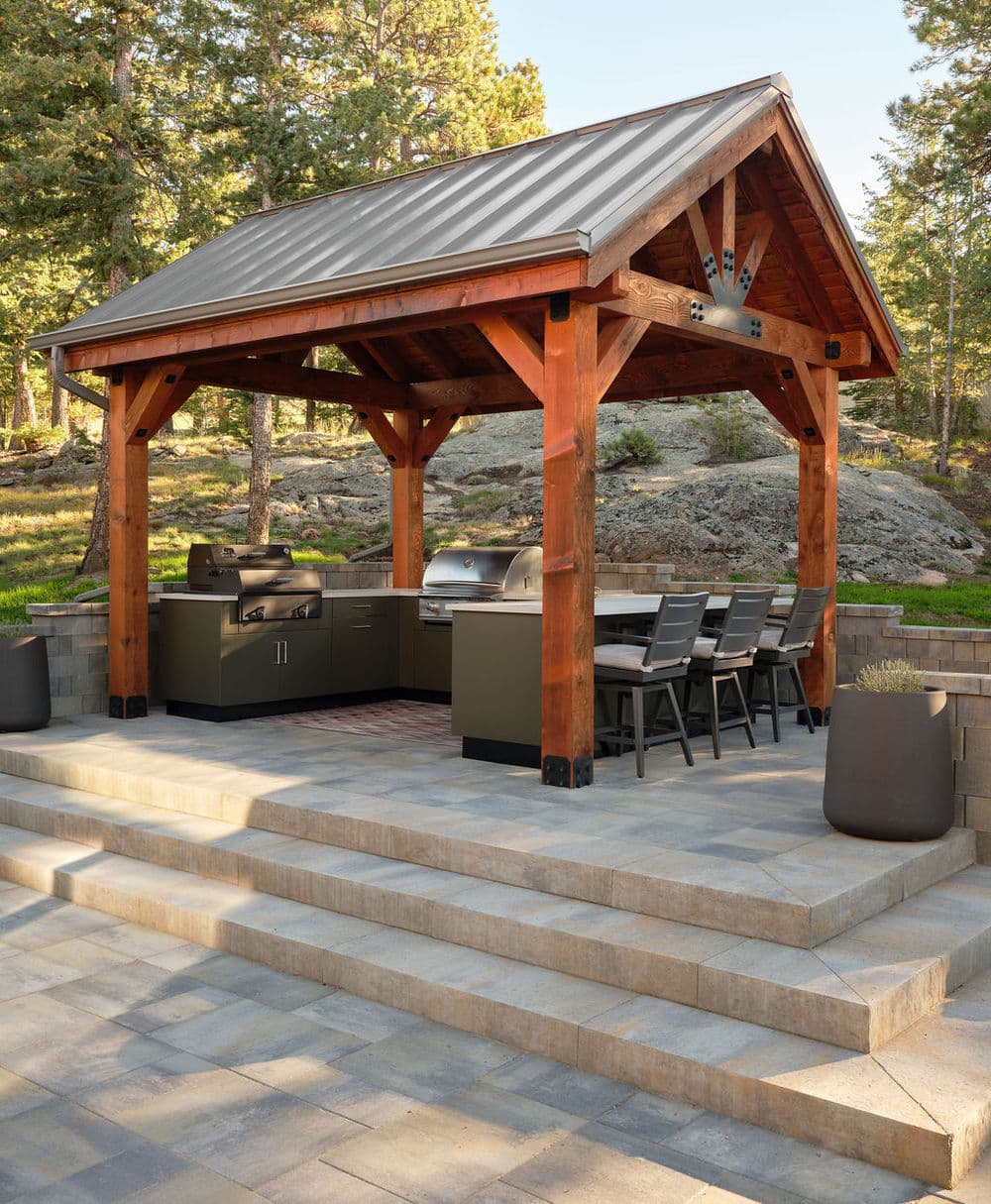 Outdoor kitchen with covered patio, grill station, and seating area in natural setting.